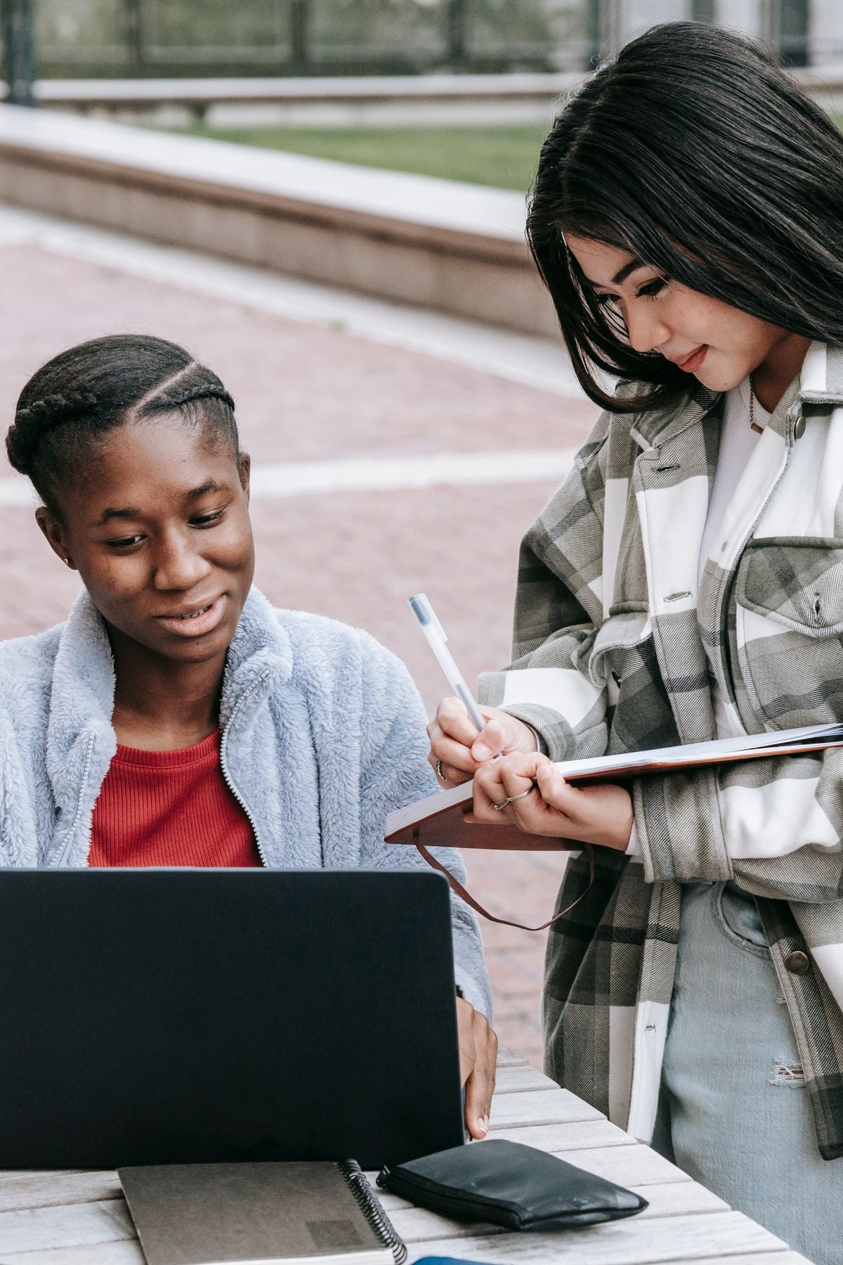 Two students collaborating with a laptop and notebook outdoors
